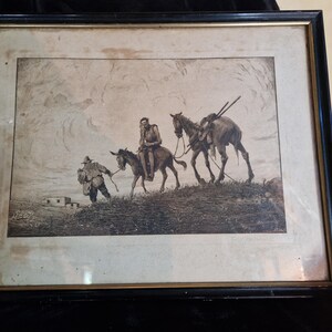 May include: A framed sepia-toned etching depicting a person leading a donkey with a rider, followed by a horse carrying long poles across a hilly landscape. The artwork is enclosed in a black frame with a thin gold inner border and a light mat.