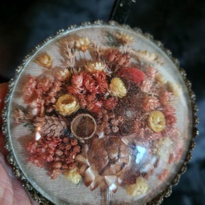 May include: A vintage, round glass pendant with a dried flower arrangement. The arrangement features various dried flowers in shades of red, yellow, and brown, encased in a clear glass dome with a decorative metal frame.
