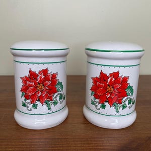 May include: A pair of white ceramic salt and pepper shakers with a green trim and a red poinsettia design.