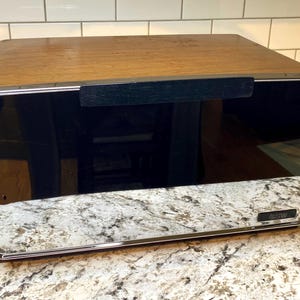 Op de afbeelding: Een vintage aanrechtapparaat met een houtlook bovenkant, een zwart voorpaneel en een chromen afwerking. Het apparaat heeft een handvat en een reflecterend oppervlak. De onderkant heeft een chromen afwerking met de letters "BSW".