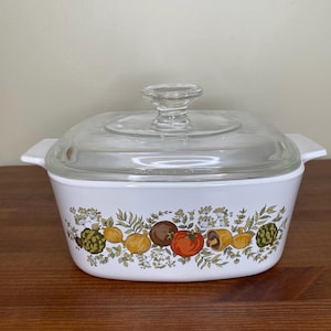 May include: White ceramic baking dish with a glass lid. The dish features a floral pattern with green leaves, yellow and orange vegetables, and brown mushrooms.