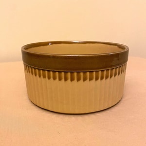 Op de afbeelding: Een bruine en beige keramische bakvorm met een geribbeld ontwerp. De vorm is rond en heeft een brede rand.