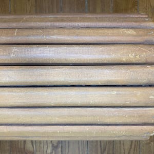 May include: Close-up of a light brown wooden bench with a slatted design. The bench has a weathered appearance with visible wood grain and minor imperfections, suggesting age and use. The design is simple and rustic.
