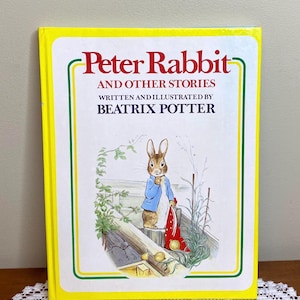 May include: A hardcover book titled "Peter Rabbit and Other Stories" by Beatrix Potter. The cover features a yellow border with green and white accents. The illustration shows Peter Rabbit in a blue jacket.
