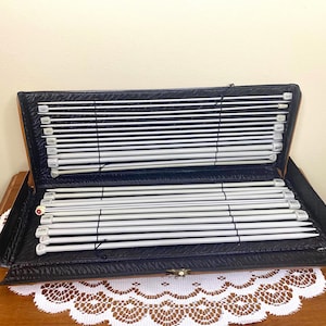 May include: A black case filled with a set of white knitting needles. The needles are organized by size and are labeled with numbers.