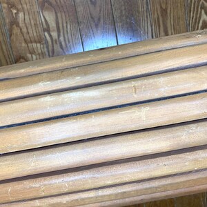 May include: A close-up of several light brown wooden dowels arranged in parallel. The dowels are cylindrical and appear to be made of natural wood. The wood grain is visible, and there are small holes drilled into the ends of some of the dowels.