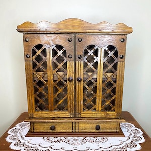 May include: A wooden cabinet with two doors and two drawers. The doors have a lattice design and are closed. The cabinet is brown and has a distressed finish.