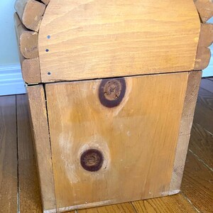 May include: A light brown wooden storage box. The box has a rectangular shape with a curved top. The wood grain is visible, and the box appears to be handmade. The box has two large knots on the front.