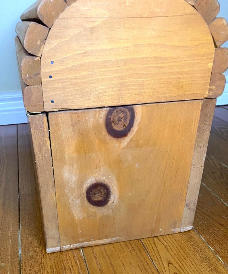 May include: A light brown wooden storage box. The box has a rectangular shape with a curved top. The wood grain is visible, and the box appears to be handmade. The box has two large knots on the front.
