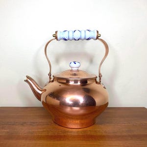 May include: A copper kettle with a white porcelain handle and lid. The kettle has a shiny, polished finish and a rounded body.