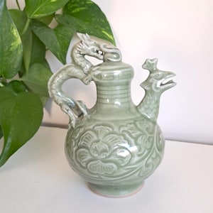 Könnte beinhalten: Eine weiße Keramik-Tasse mit schwarzem Henkel und dem Text "But First, Coffee" in fetter, schwarzer Schrift. Die Tasse steht vor einem neutralen Hintergrund, der ihr schlichtes Design hervorhebt.