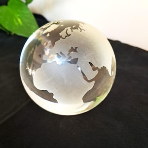 Peut inclure: Une sphère en verre transparent présentant une carte du monde gravée et dépolie. Les continents sont représentés avec une finition blanche mate sur le corps sphérique transparent, mettant en évidence la géographie de l'Afrique et de l'Europe.