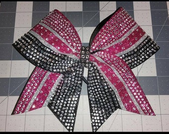 May include: A large black and pink cheer bow with silver glitter stripes. The bow is covered in rhinestones.