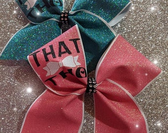 May include: Two cheer bows with glitter fabric. The top bow is teal with white trim and the text "I'm just that tho". The bottom bow is pink with white trim and the text "That tho".