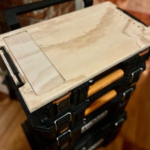 May include: A black tool chest with a wooden top. The top has a rectangular cutout and is secured with screws. The chest has multiple drawers and is on wheels.