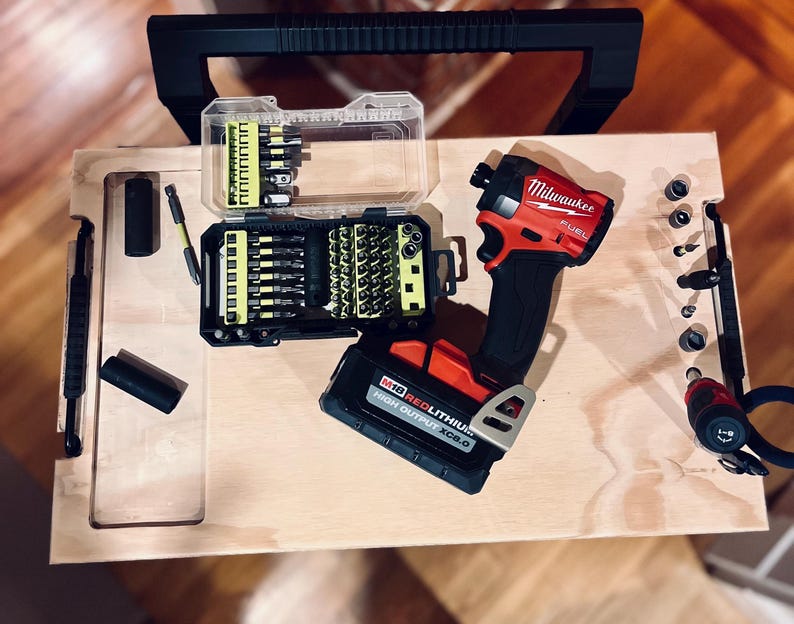 Op de afbeelding: Een rode en zwarte draadloze boormachine met een Milwaukee FUEL-label, een rode lithium-accu en een koffer met verschillende boorbits.