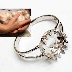 May include: A silver ring with a round bezel setting. The bezel is ornate and has a raised edge. The ring is designed to hold a cabochon stone.