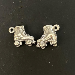 Pode incluir: Dois pingentes de patins de rodas de prata com um laço para prender a um bracelete ou colar.
