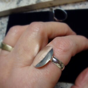 May include: A silver ring with a half-circle design. The ring is worn on a person's finger.