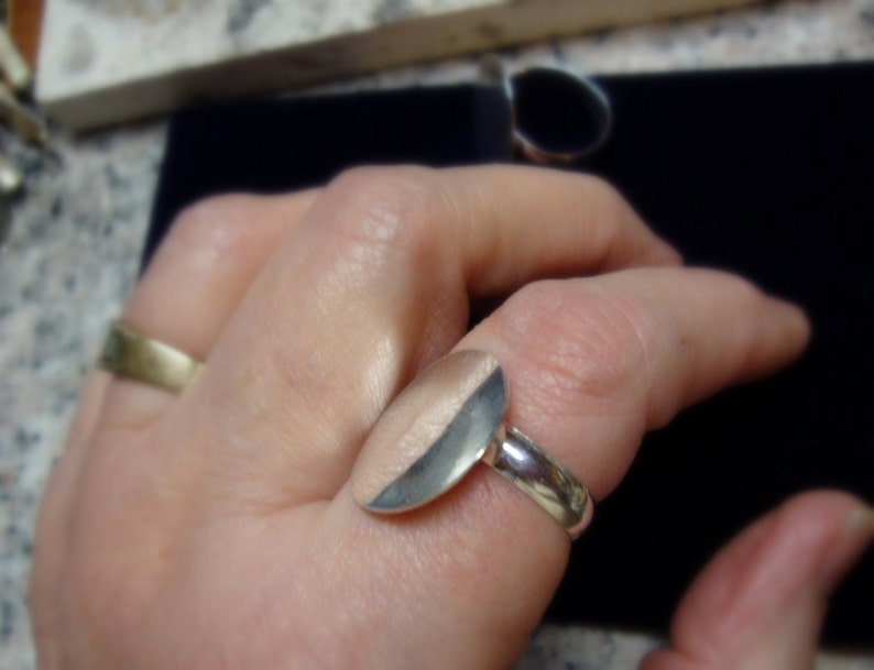 May include: A silver ring with a half-circle design. The ring is worn on a person's finger.