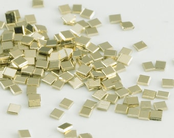 May include: A pile of small, gold-colored, square-shaped metal pieces. The pieces are scattered on a white surface.