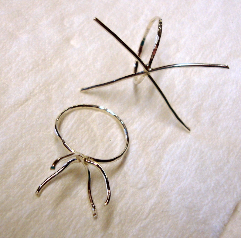 May include: Two silver ring settings for jewelry making. One setting is a round bezel with prongs, the other is a six-prong setting.
