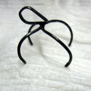 May include: A black metal hair clip with a unique design. The clip has a loop at the top and two prongs that extend out from the loop.