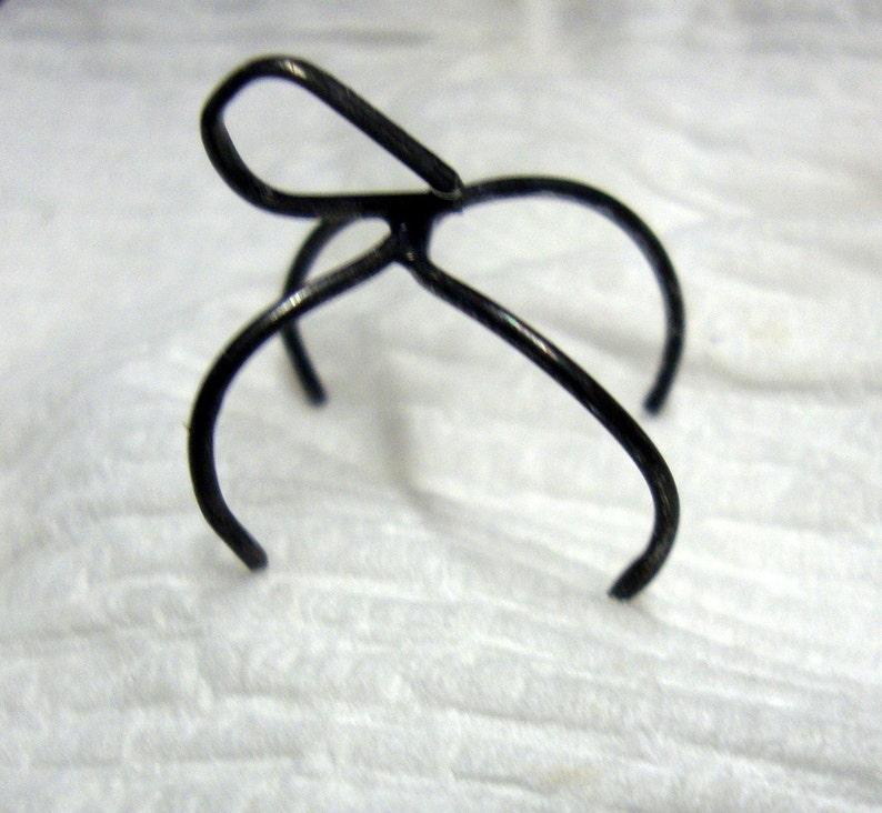 May include: A black metal hair clip with a unique design. The clip has a loop at the top and two prongs that extend out from the loop.