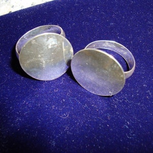 May include: Two silver rings with round, flat tops. The rings are on a blue velvet surface.