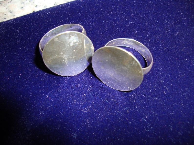 May include: Two silver rings with round, flat tops. The rings are on a blue velvet surface.