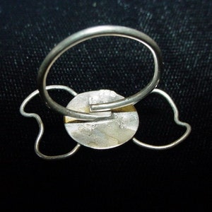 Op de afbeelding: Zilveren ring met een rond, getextureerd middenstuk en twee hartvormige draadlussen aan beide zijden.