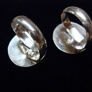 May include: Two silver rings with oval-shaped settings. The rings are shown from the back, revealing the smooth, silver bands.