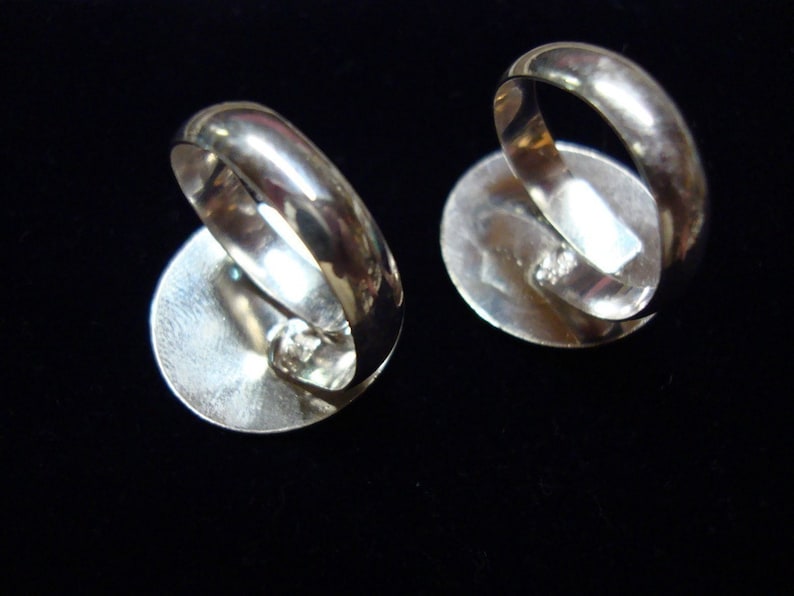 May include: Two silver rings with oval-shaped settings. The rings are shown from the back, revealing the smooth, silver bands.