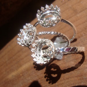 May include: Silver ring with three crown-shaped settings for stones. The ring is twisted and has a delicate design.