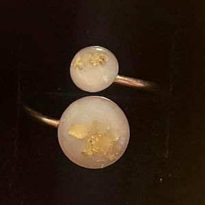 May include: A gold ring with two white resin round stones embedded with gold flakes.