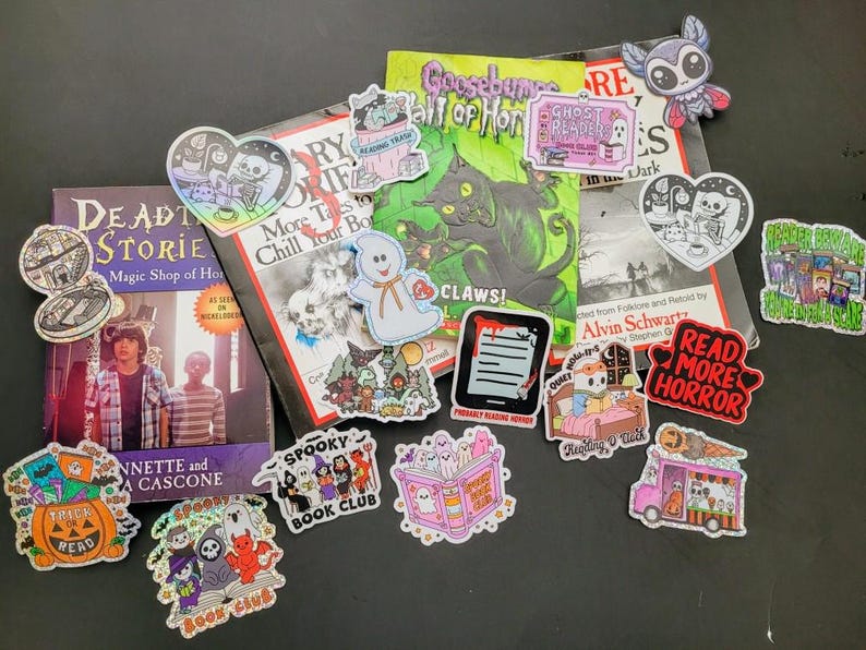 May include: A collection of stickers and books with a spooky theme. The stickers feature ghosts, bats, and other Halloween-related imagery. The books include titles like "Deadly Stories" and "Goosebumps".