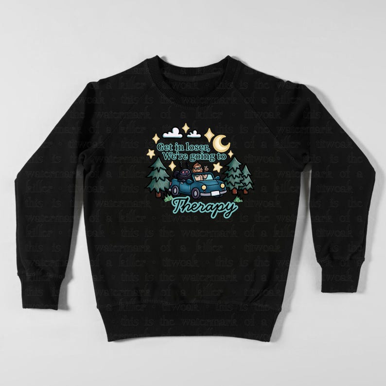 May include: Black sweatshirt with a whimsical graphic. The design features a blue car with passengers, trees, stars, and a crescent moon. Text reads "Get in loser, We're going to Therapy."