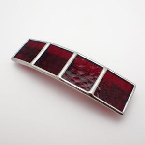 May include: A rectangular hair barrette featuring four distinct segments of deep red stained glass. Each glass panel is encased in a smooth, silver-toned metal frame, creating a structured and geometric accessory with a polished finish.