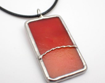 May include: A red and orange stained glass pendant with a silver wire design, hanging from a black leather cord.