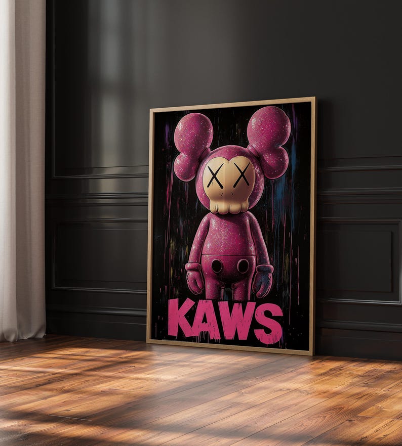 May include: A framed artwork featuring a pink KAWS figure with crossed-out eyes and a skull-like face. The figure has large, rounded ears and gloved hands. The word "KAWS" is printed in pink at the bottom. The artwork is set against a black background.
