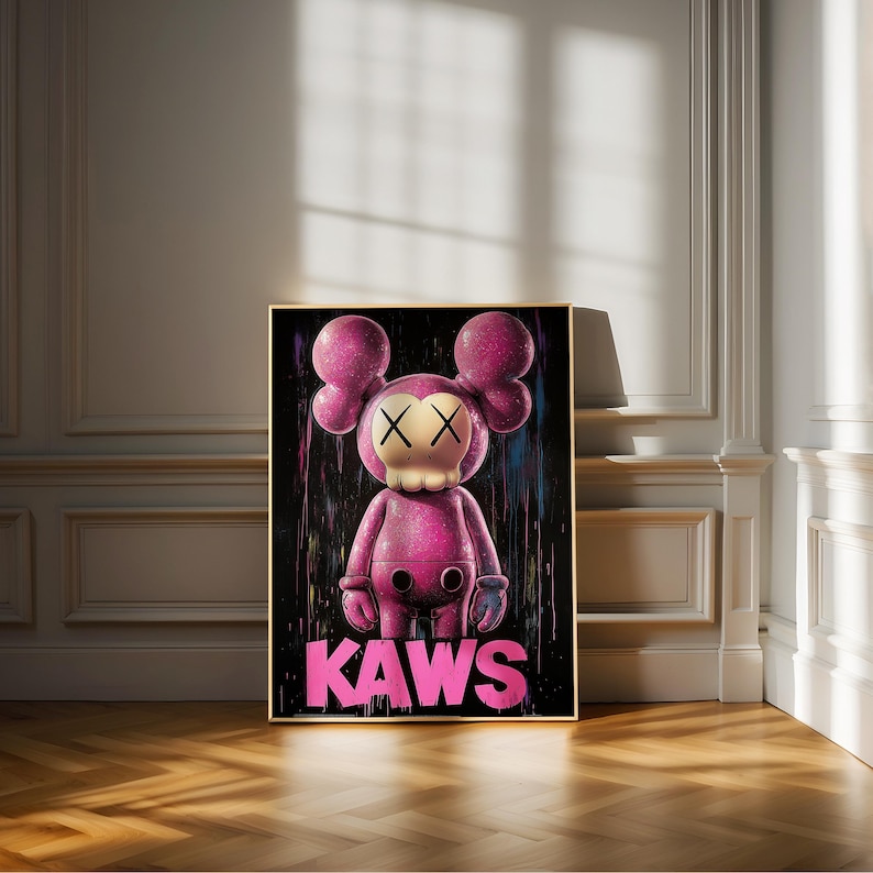 May include: A framed artwork featuring a pink KAWS figure with crossed-out eyes and a skull-like face. The figure stands against a black background with colorful paint drips. The word "KAWS" is written in pink at the bottom.