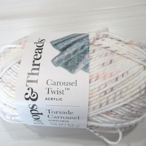 May include: A skein of Loops & Threads Carousel Twist acrylic yarn. The yarn is primarily white with flecks of peach, tan, and gray. The label reads "Carousel Twist" and "Acrylic".
