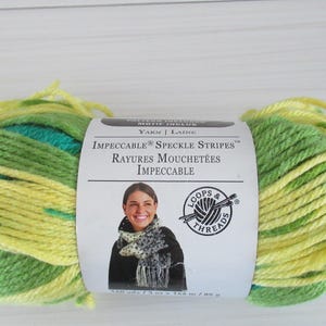 Puede incluir: Un ovillo de hilo Loops & Threads Impeccable Speckle Stripes en amarillo y verde. La etiqueta dice "Impeccable Speckle Stripes, Rayures Mouchetées Impeccable".