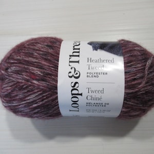 以下が含まれることがあります： バーガンディ、グレー、ブラックのカラーブレンドのLoops & Threads Heathered Tweedの毛糸玉。ラベルには「Heathered Tweed Polyester Blend Tweed Chiné」と記載されています。糸は416ヤード/150グラムです。