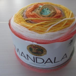 May include: A skein of Lion Brand Mandala yarn in a vibrant mix of colors, including yellow, orange, white, and pink. The yarn is wrapped in a cylindrical shape with a label that reads "Mandala".