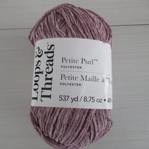 以下が含まれることがあります： Loops & Threadsの、薄紫色のPetite Purlポリエステル糸の玉。ラベルには「Petite Purl」と「Petite Maille à l'Étoffe」と記載されています。糸玉には537ヤードの糸が含まれています。