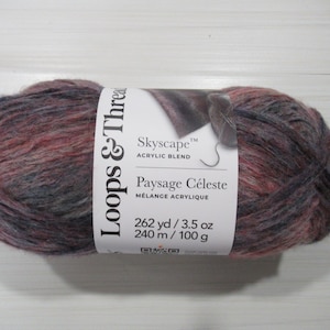 May include: A skein of Loops & Threads Skyscape acrylic blend yarn. The yarn is a mix of colors including red, gray, and purple. The label reads "Skyscape" and "Paysage Céleste". The skein contains 262 yards and weighs 3.5 ounces.
