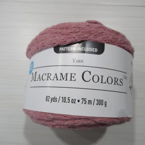May include: A ball of dusty rose macrame yarn with a white label. The label reads "Macrame Colors" and includes the text "Pattern Included". The yarn is 82 yards, 10.5 ounces, 75 meters, and 300 grams.
