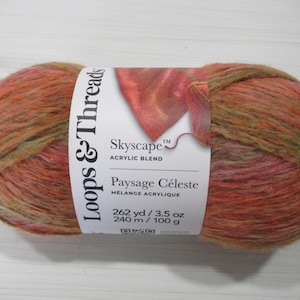 May include: A skein of Loops & Threads Skyscape acrylic blend yarn in shades of orange, pink, and green. The label reads "Paysage Céleste" and lists the yarn as 262 yards and 3.5 ounces.