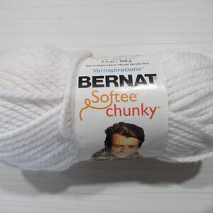Könnte beinhalten: Ein großer, weißer Knäuel Bernat Softee Chunky-Garn. Das Etikett gibt 100 g Garn an. Das Garn ist dick und weich, ideal für Strick- oder Häkelprojekte. Das Etikett zeigt den Markennamen und ein Bild einer Person.